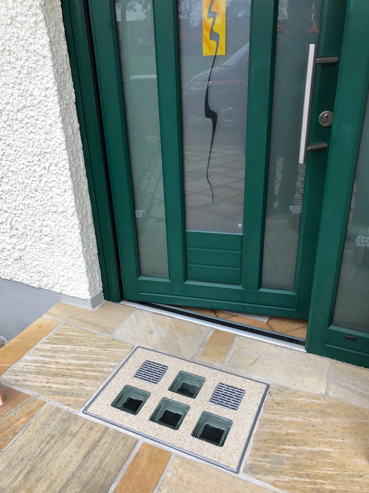 Wasserdichte Lichtschachtabdeckung mit Glasbausteinen vor grüner Haustür