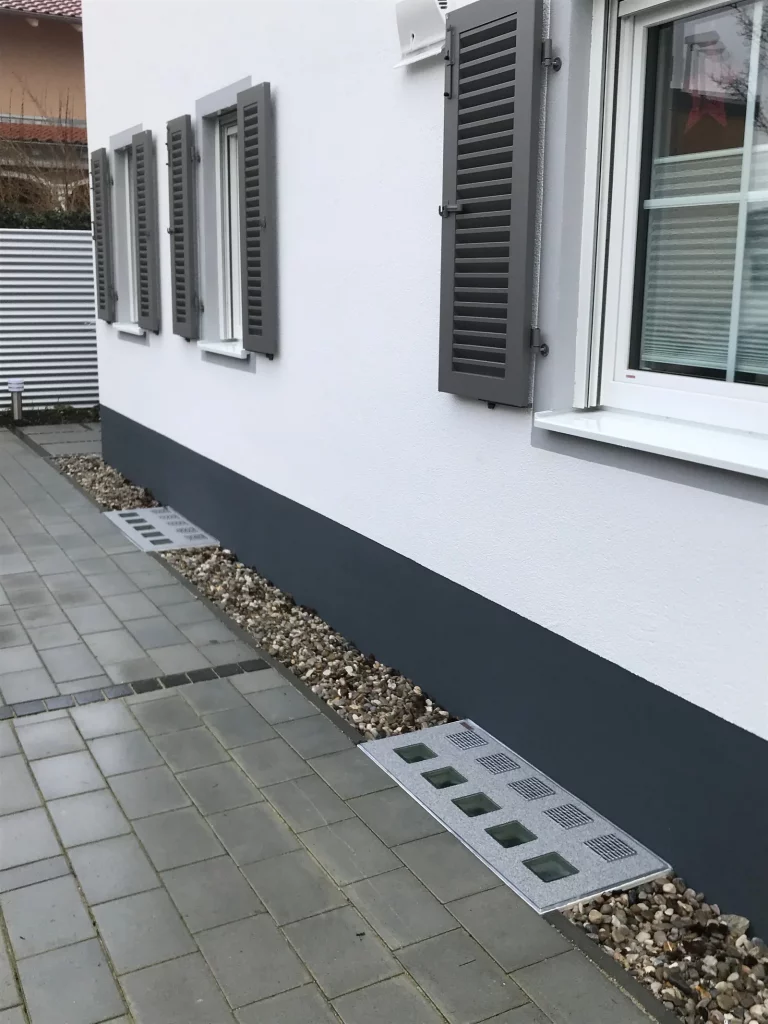 Wasserdichte Lichtschachtabdeckung mit Glasbausteinen am Sockel eines weißen Wohnhauses